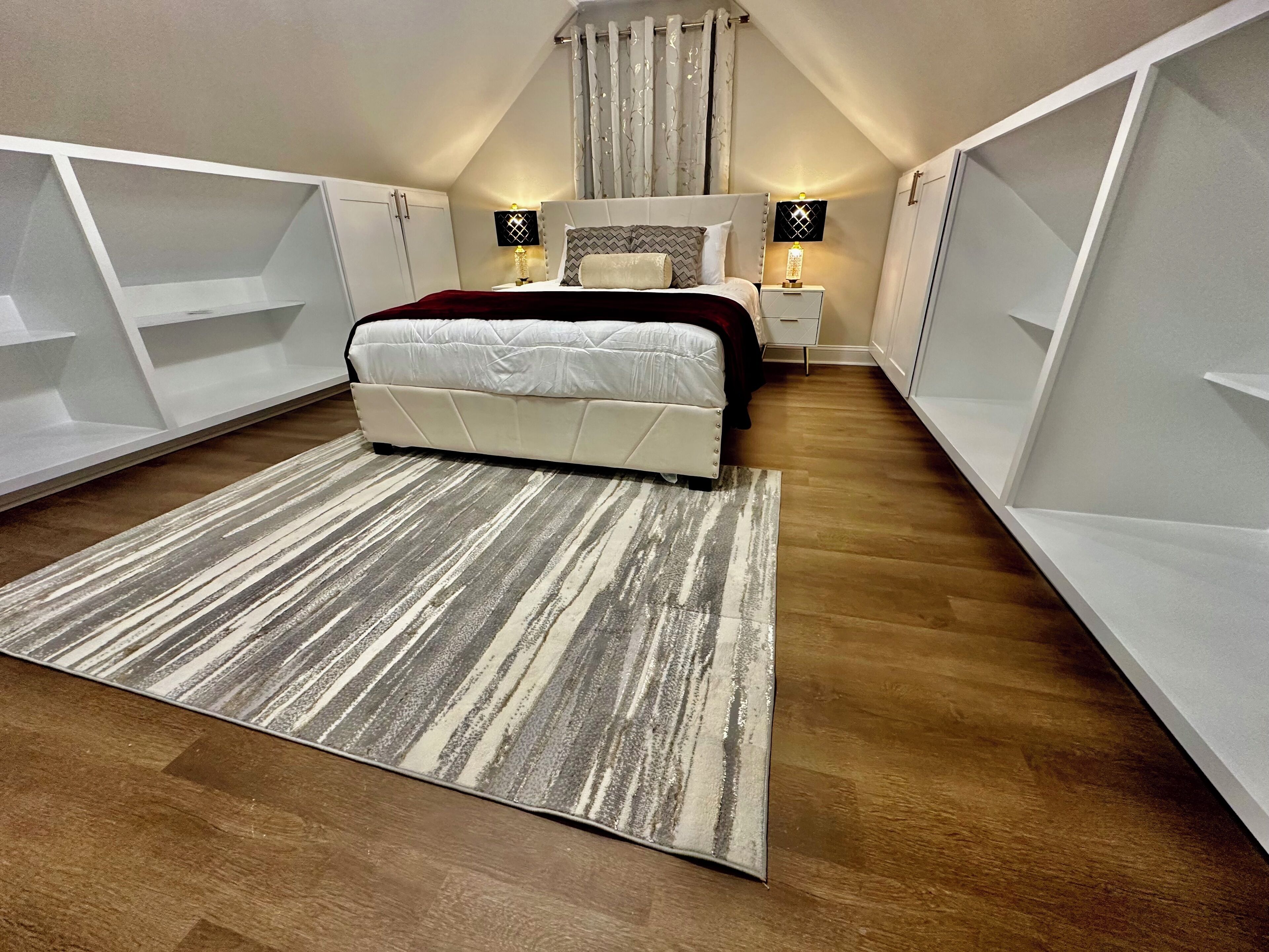 Un dormitorio con cama, mesitas de noche, un tapete y estanterías empotradas.