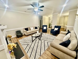 Uma sala de estar moderna com sofá, poltronas, mesa de centro e ventilador de teto.