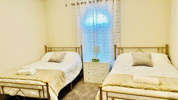 Habitación doble con dos camas individuales, una mesita de noche, una lámpara y una ventana con cortinas estampadas.