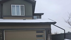 Ein zweistöckiges Haus mit Garage, Steinverkleidungen und einem mit Schnee bedeckten Dach.