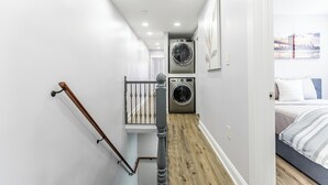 Ein enger Flur mit einer Treppe, die zu einem Schlafzimmer führt. Im Hintergrund ist eine Waschmaschine zu sehen.