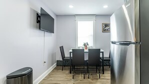 Eine kompakte Küche mit Edelstahlkühlschrank, einem an der Wand montierten Fernseher und einem Essbereich mit Tisch und Stühlen.