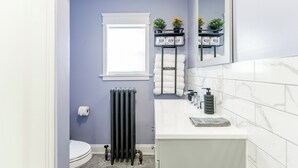 Ein Badezimmer mit Toilette, schwarzem Heizkörper, Waschbecken mit Marmorplatte und einem Spiegel über dem Waschbecken.
