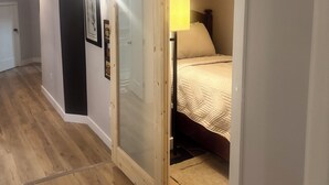 Ein Schlafzimmer mit einem Bett, einem Nachttisch, einer Lampe und einer Schiebetür zu einem anderen Raum.