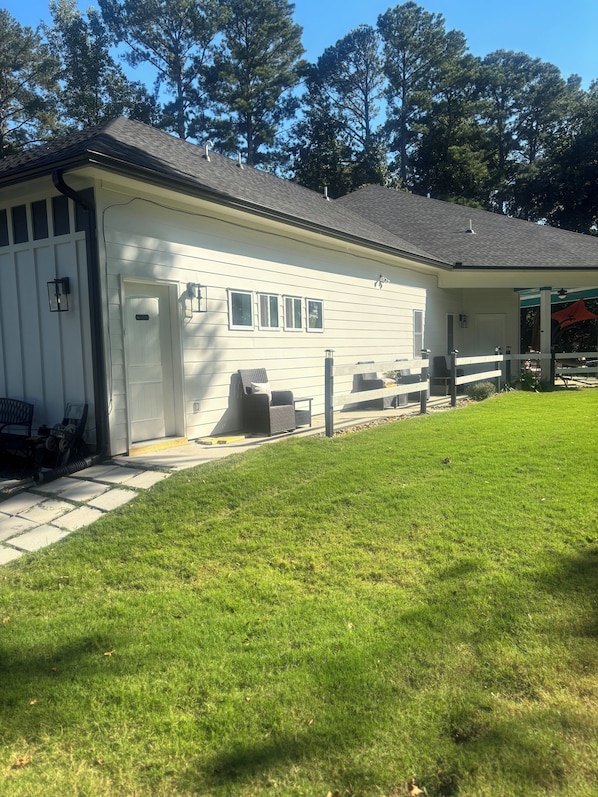 A white building with a porch, a covered outdoor seating area, and a grassy lawn.
