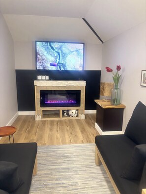 A modern living room with a fireplace, a flat-screen TV mounted above it, and a black sofa.