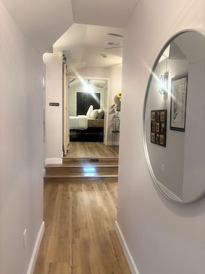A hallway leading to a bedroom with a bed, a mirror, and a framed picture on the wall.