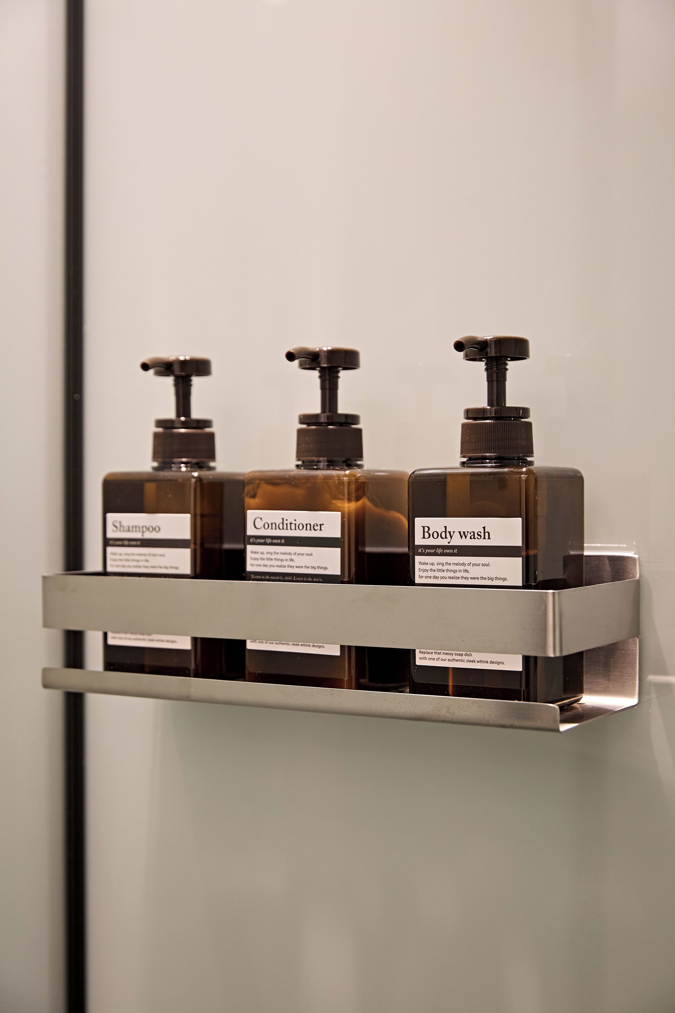 A bathroom shelf with three bottles of shampoo, conditioner, and body wash.