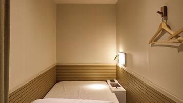 A narrow hotel room with a single bed, a bedside table, and a wall-mounted hanger.