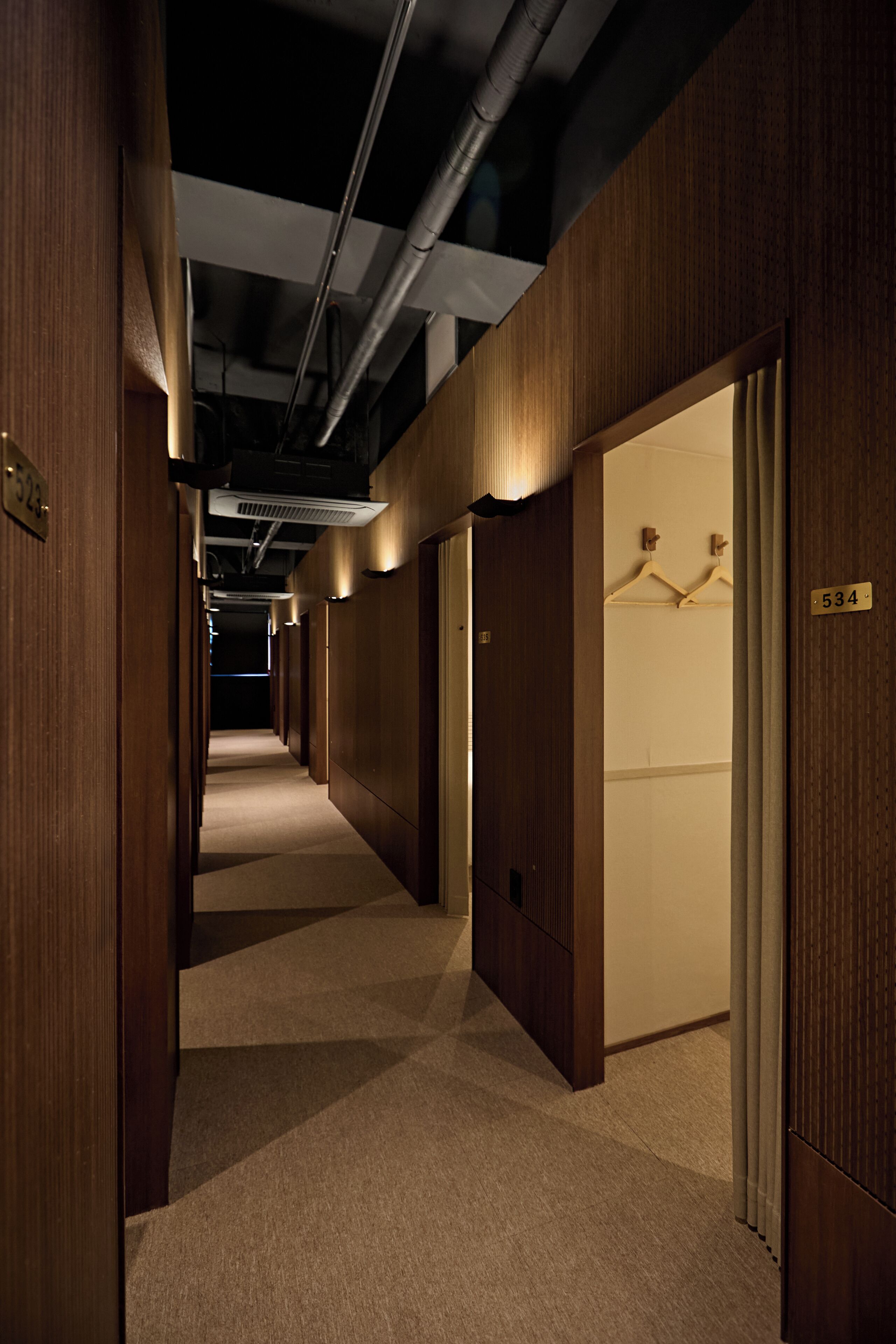 A corridor with wooden walls and doors, each marked with a number.