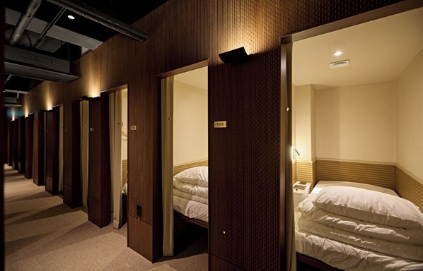 A hotel corridor with wooden walls and doors, leading to individual rooms with beds and headboards. - Kiwa Hostel (Seoul)