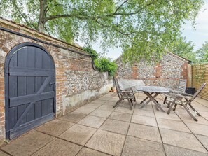 An outdoor patio with a stone wall, a wooden table, and two wooden chairs. - Sparrows Nest - UK50109 (Sparrow Green, near Dereham)