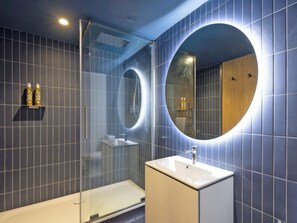 Ein modernes Badezimmer mit einer gläsernen Duschkabine, einem runden Spiegel und einem weißen Waschbecken.