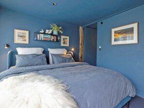 A bedroom with a bed, pillows, a white fluffy rug, a shelf with books and a plant, and two framed pictures on the wall. - Sparrows Nest - UK50109 (Sparrow Green, near Dereham)