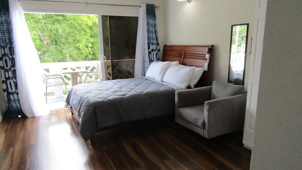 Une chambre à coucher avec un lit, une chaise, une table et une vue sur la verdure à l’extérieur.