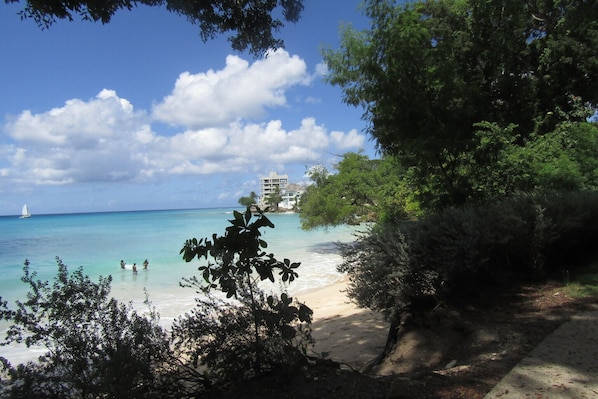 A beach with clear turquoise water, a sandy shore, and a building in the background.