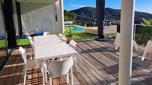 A covered outdoor area with a table and chairs, a pool, and a view of a mountainous landscape.