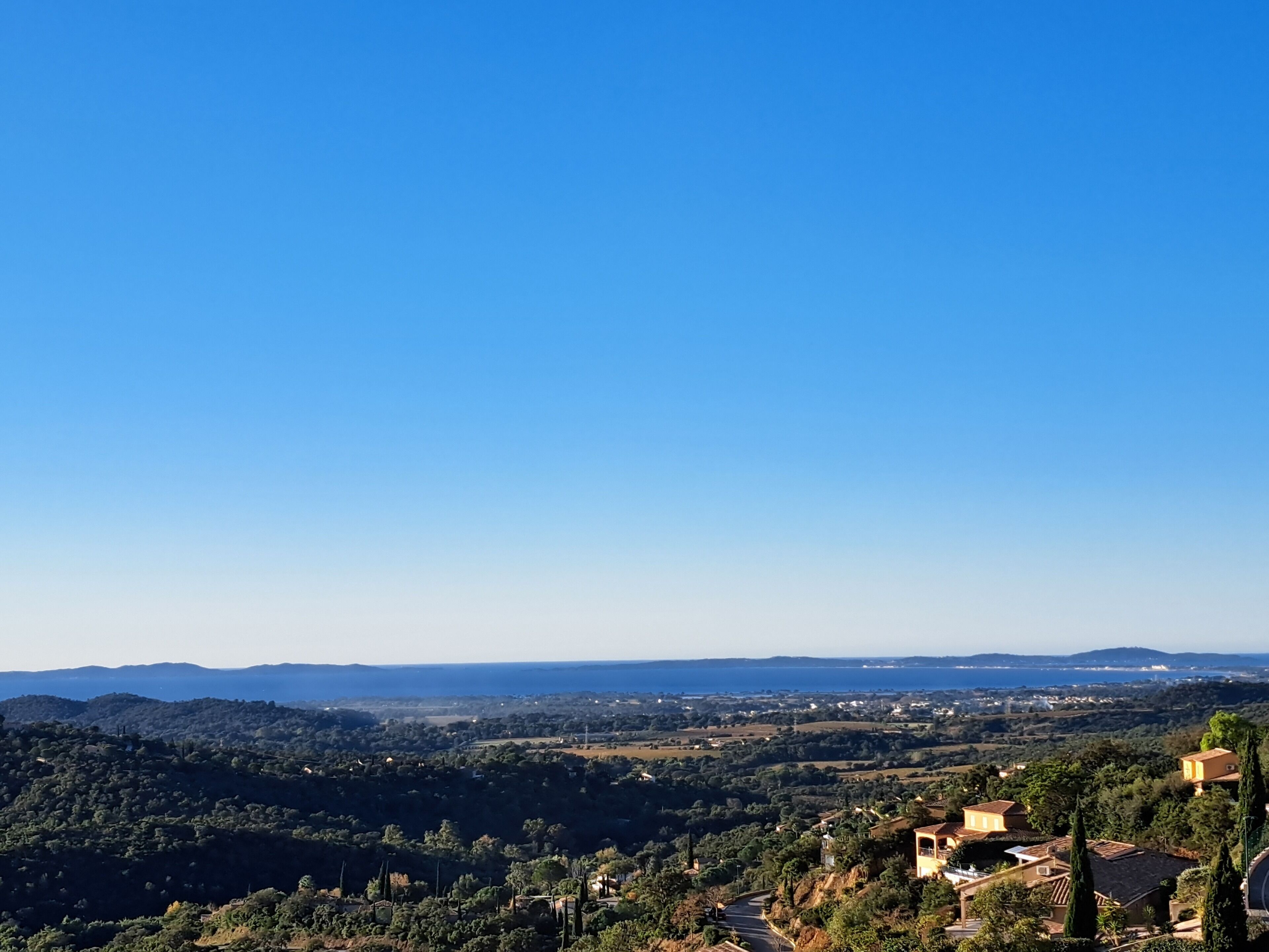 A panoramic view of a coastal landscape with rolling hills, scattered houses, and a clear blue sky.