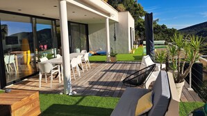 A modern outdoor patio with a wooden deck, white furniture, and a green lawn.