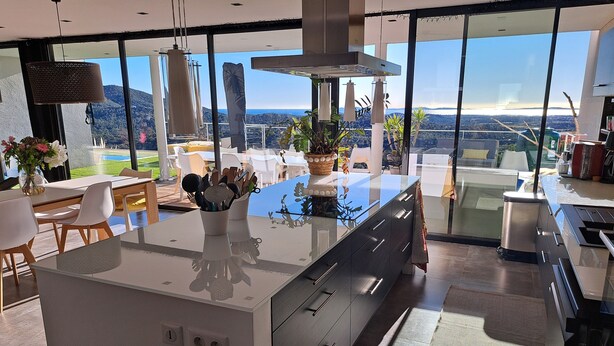 A modern kitchen with a large island, large windows, and a view of the landscape.
