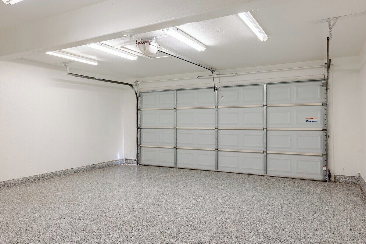 A clean, empty garage with a closed garage door, fluorescent lighting, and a concrete floor.