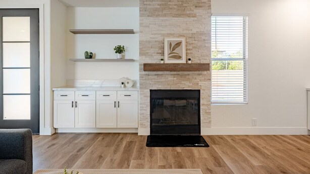 A modern kitchen with white cabinets, a stone accent wall, a fireplace, and a window with blinds. - Modern, Spacious & Peaceful 4B/3B House (Chandler)