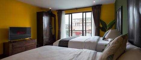 A hotel room with two beds, a TV, a wardrobe, and a large window with curtains.