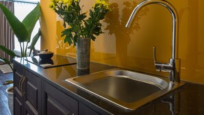 A modern kitchen with a stainless steel sink, dark cabinetry, and a yellow accent wall. - Centraltique Downtown Living (Hanoi)