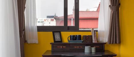 A room with a yellow wall, a window with curtains, a desk with a chair, and a bed.
