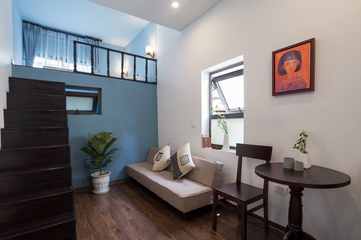 Uma sala de estar moderna com um sofá, uma mesa de jantar, uma escada e um quadro na parede.