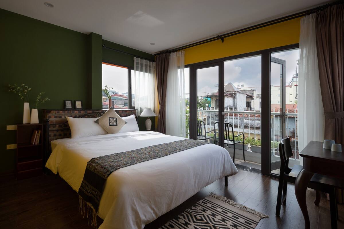 Quarto de hotel moderno com uma cama grande, uma varanda com vista e um espaço de refeições.