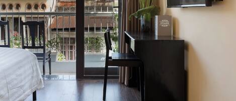 A hotel room with a bed, a desk with a chair, a television, and a view of the city through a large window.