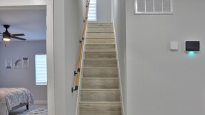 A staircase with wooden steps and a handrail, leading to a room with a bed and a ceiling fan.