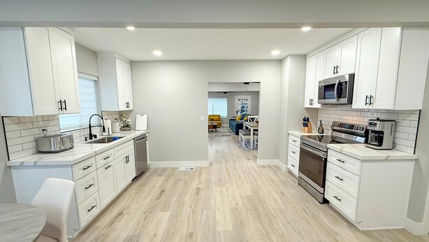 A modern kitchen with white cabinets, a microwave, oven, and a dining area with a table and chairs.