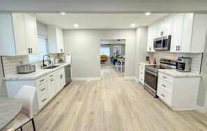 Una cucina moderna con mobili bianchi, un forno a microonde, forno e una zona pranzo con tavolo e sedie.