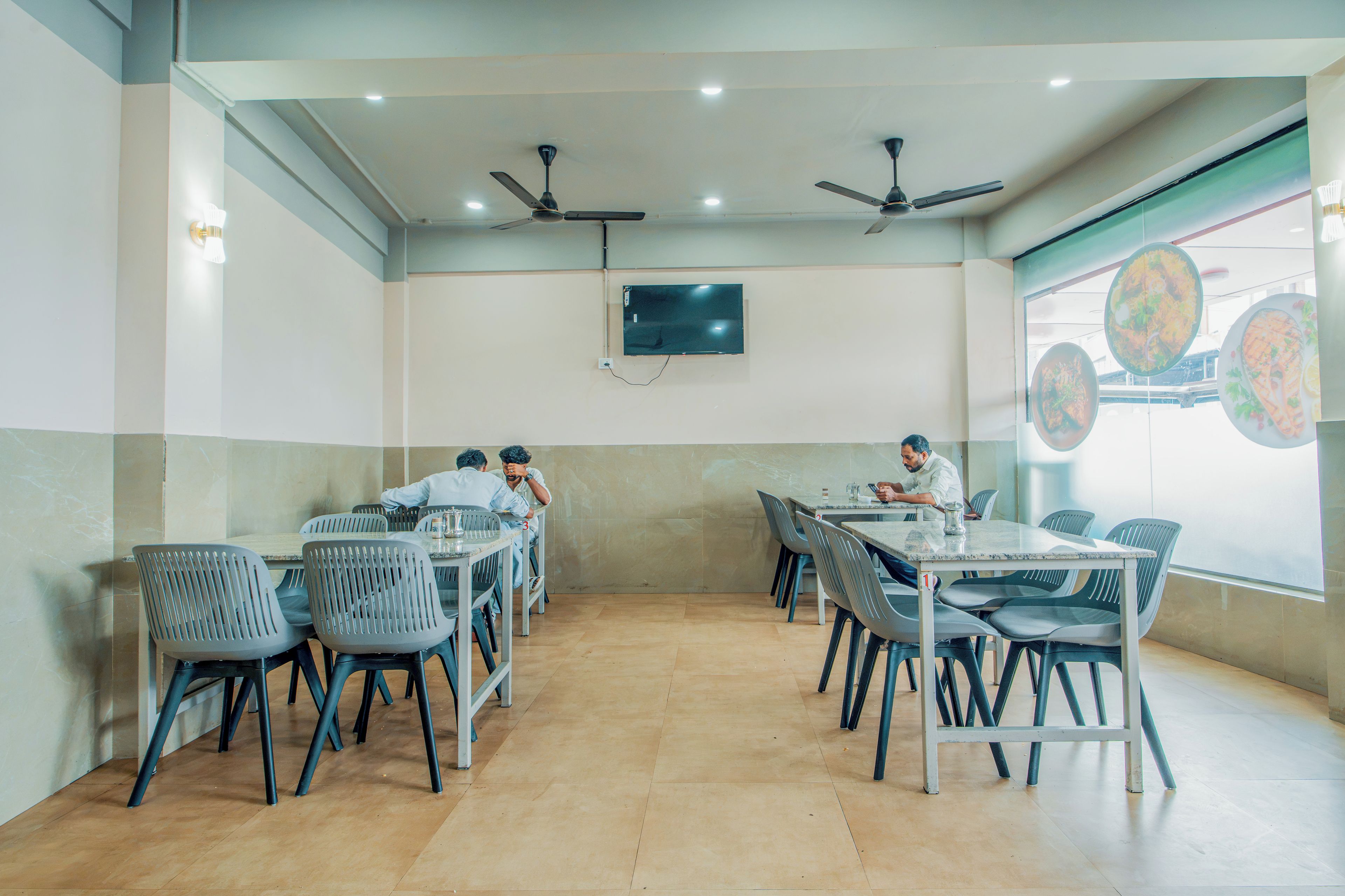 Une salle de conférence équipée de tables et de chaises, d’un téléviseur à écran plat fixé au mur et de ventilateurs de plafond.