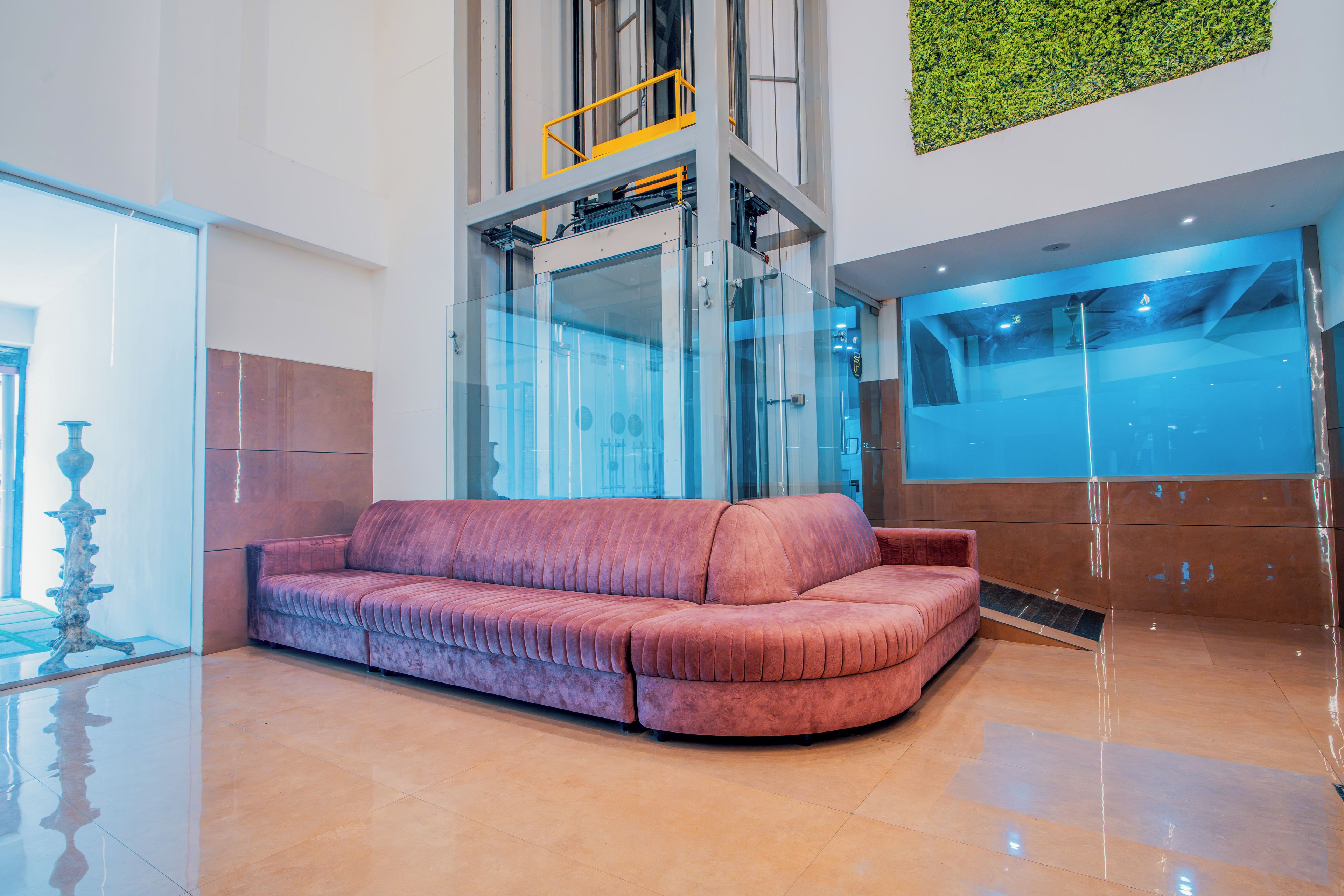 A modern lobby with a curved sofa, a glass elevator, and a green wall feature.