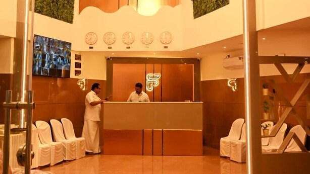 A hotel reception area with a modern design, including a reception desk, seating area, and decorative elements like a chandelier and wall-mounted clocks. - HOTEL SOUTH FOREST (Sulthan Bathery)