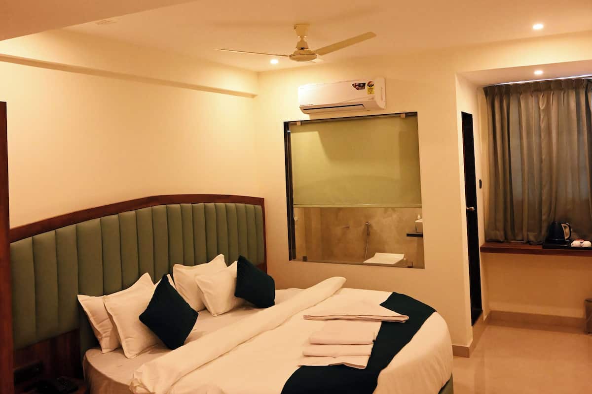 Une chambre d’hôtel avec un lit rond, un ventilateur de plafond, un miroir et une salle de bain visible à travers une paroi en verre.
