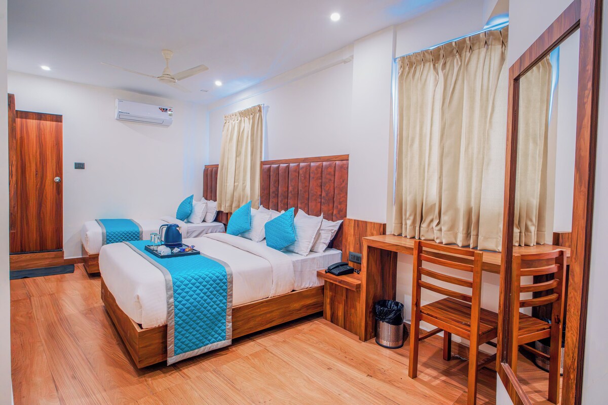 A hotel room with two beds, a wooden headboard, a desk, a chair, a telephone, and a waste bin.
