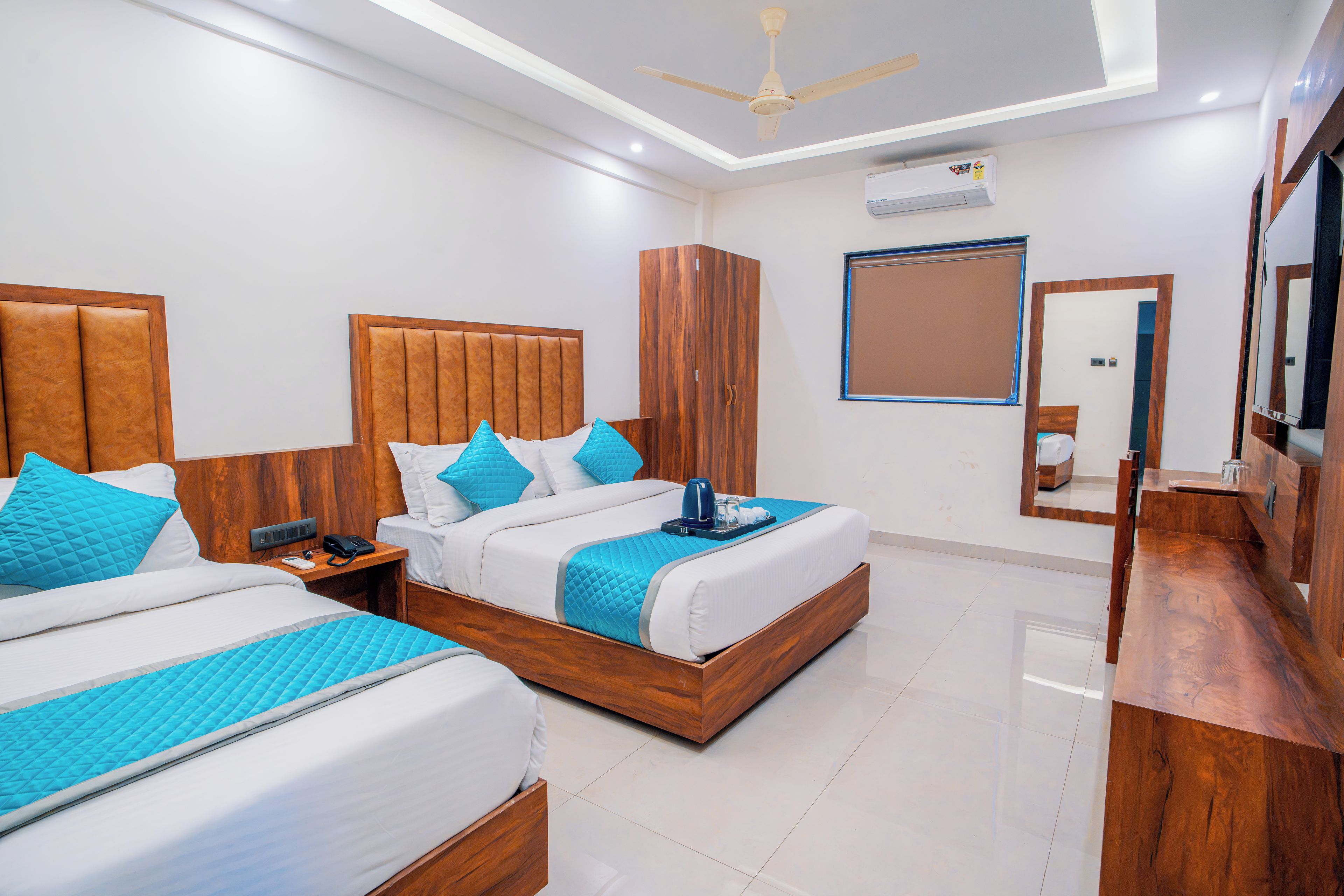 Quarto de hotel com duas camas, um guarda-roupa, um ventilador de teto e um espelho grande.