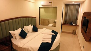 A modern hotel room with a curved bed, a large mirror, a television, and a window with curtains. - HOTEL SOUTH FOREST (Sulthan Bathery)