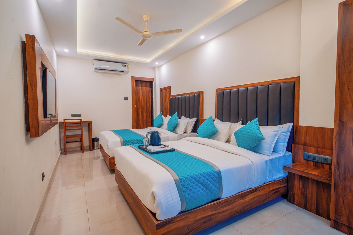 A hotel room with a large bed, bedside tables, a desk, a chair, a ceiling fan, and an air conditioning unit.