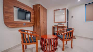 A room with two wooden chairs, a small round table, a TV mounted on a wooden wall, a wardrobe, and a mirror.