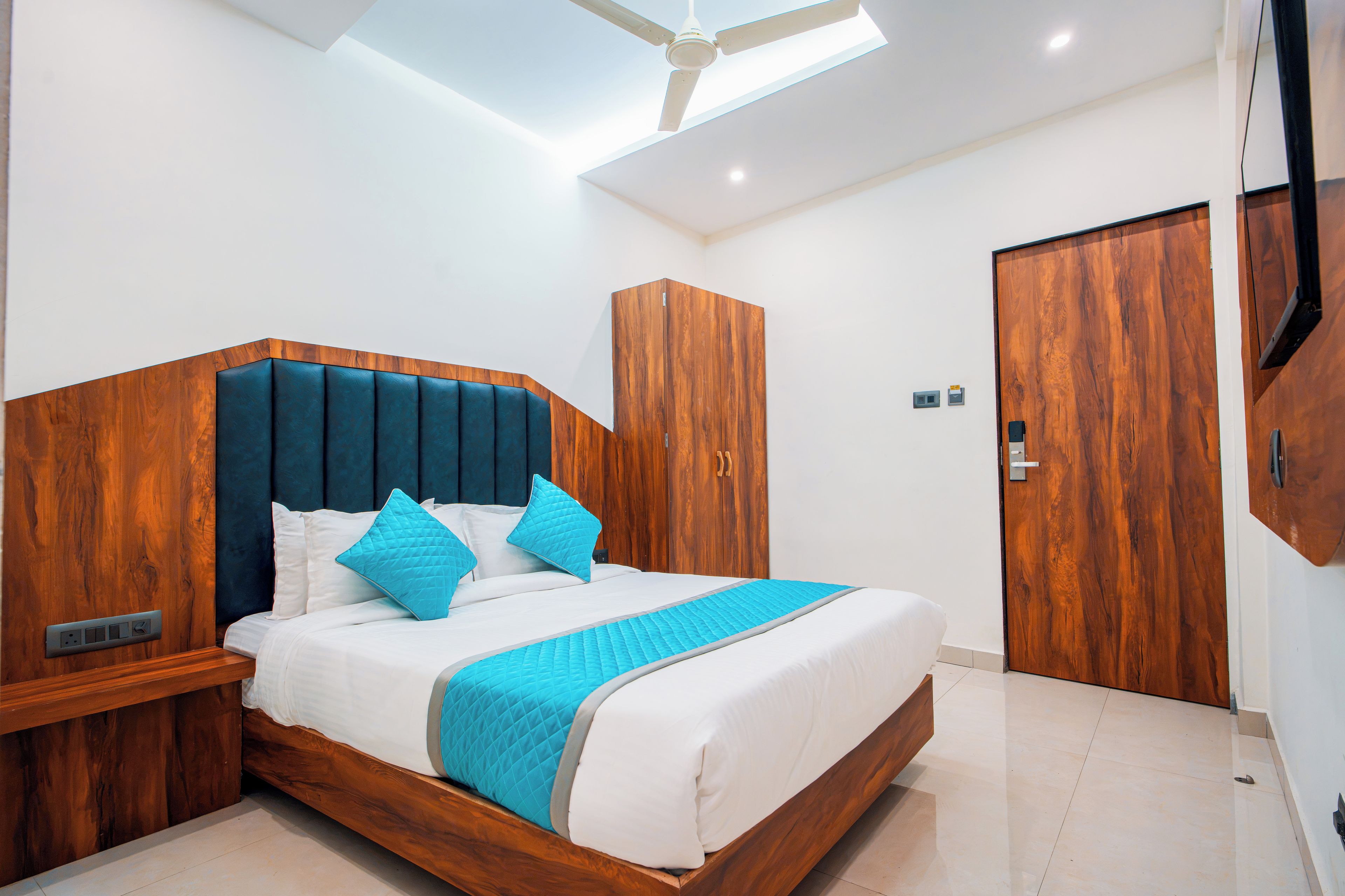 Une chambre moderne avec une tête de lit en bois, un lit avec une literie blanche et des touches de bleu, une armoire et un ventilateur de plafond.