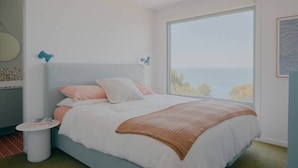 A bedroom with a large window, a bed with white and pink bedding, and a small bedside table. - Iluka Bach - Beautiful sea views at Wye (Wye River)