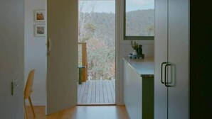 A modern kitchen with a wooden floor, a view of a forested area, and a small seating area with a chair. - Iluka Bach - Beautiful sea views at Wye (Wye River)