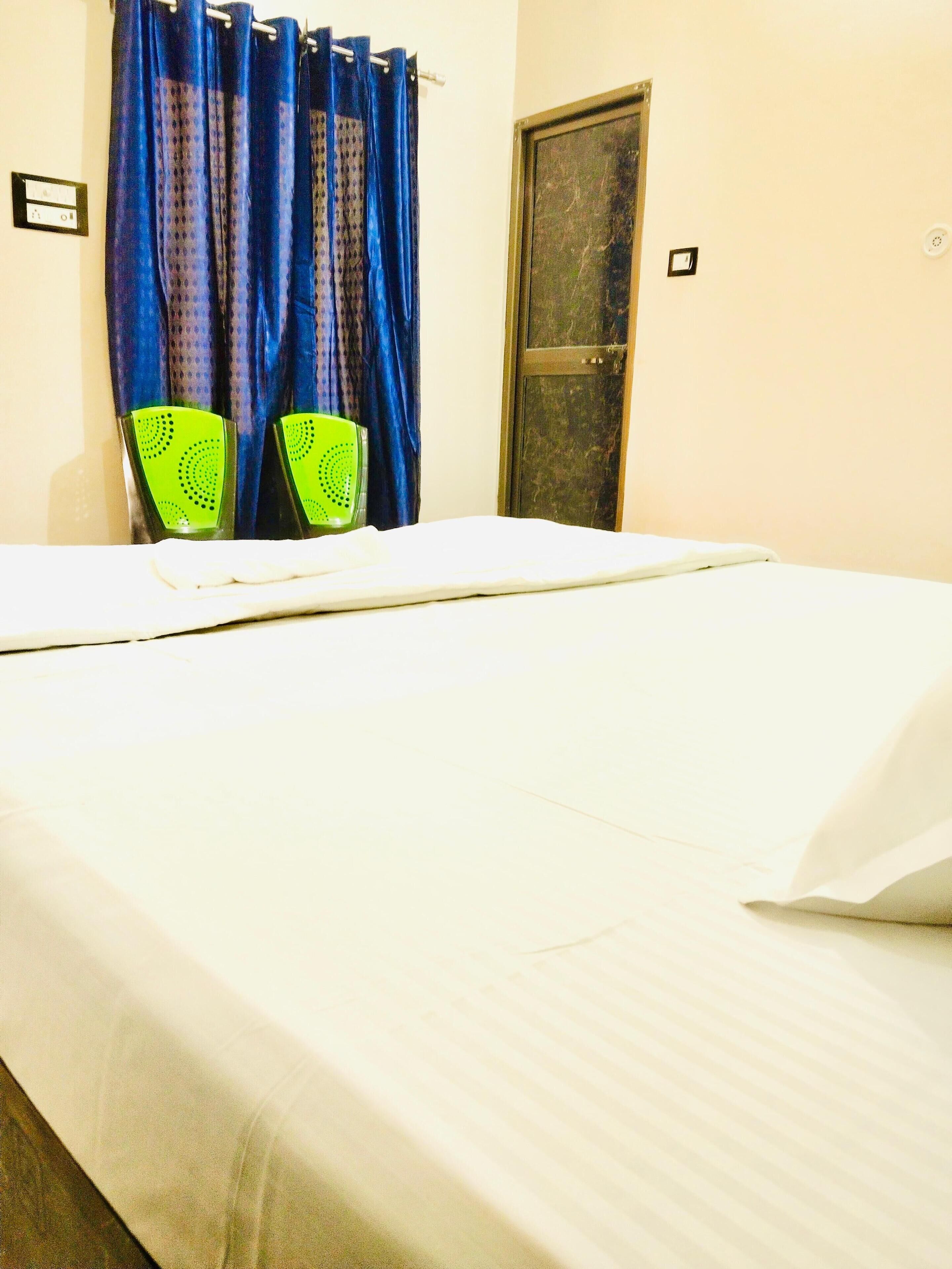 A bed with white bedding, a blue curtain, and two green chairs with heart patterns.