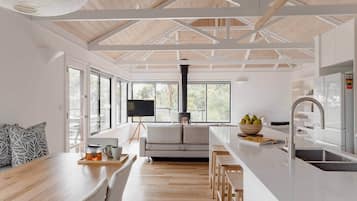 A modern kitchen with a central island, a dining area with a wooden table and chairs, and large windows providing natural light.