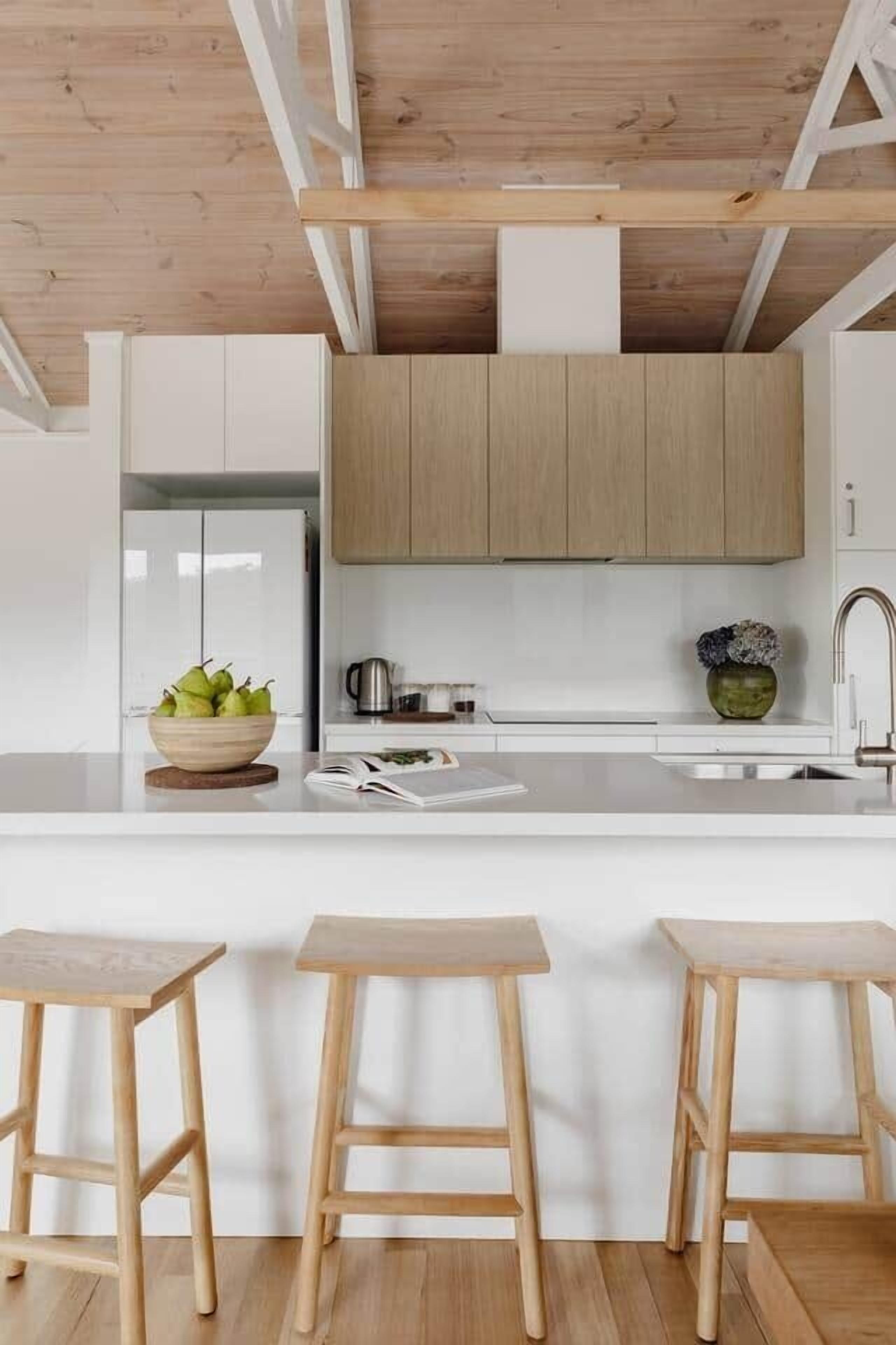 A modern kitchen with wooden cabinets, a white countertop, and three wooden stools.